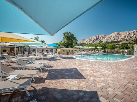 Zwembadzone met ligbedden en kleurrijke parasols bij Valamar Camping Baška, Primorje-Gorski Kotar, Kroatië.