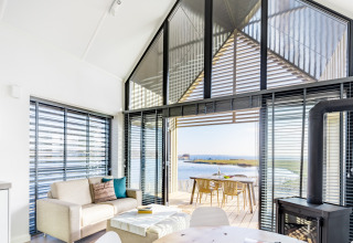 Lichte woonkamer met modern interieur, grote ramen en uitzicht op het water bij Oesterdam Resort in Zeeland.