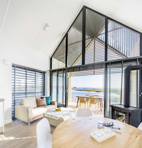 Lichte woonkamer met modern interieur, grote ramen en uitzicht op het water bij Oesterdam Resort in Zeeland.