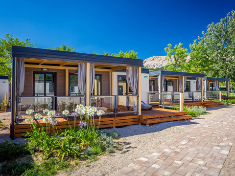 Moderne Lodges bei Vela Bay Home mit Holzterrassen, Blumen und klarem Himmel an einem sonnigen Tag.