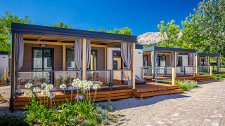 Moderni lodge al Vela Bay Home con terrazze in legno, aiuole fiorite e cielo azzurro limpido.