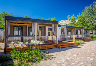 Moderne Vela Bay Home lodges met houten terrassen, bloemperken en een heldere blauwe lucht.