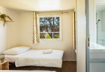 Chambre lumineuse avec deux lits simples, fenêtre, rideau coloré et salle de bain au Camping Brioni, Croatie.