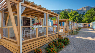 Buitenfoto van Marena Home met moderne houten lodges, kleurrijke bloemen en bergen op de achtergrond bij zonnig weer.