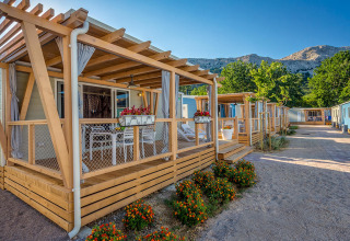 Foto exterior de Marena Home con modernas cabañas de madera, flores coloridas y montañas al fondo en un día soleado.