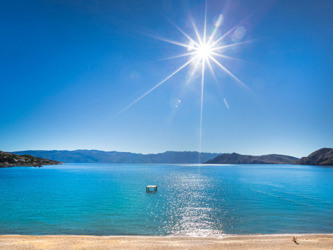 Sonniger Strand mit klarem Wasser und Bergen bei Valamar Camping Baška, Primorje-Gorski Kotar, Kroatien.