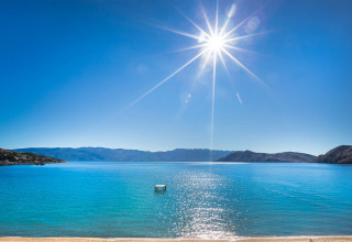 Plage ensoleillée avec eau bleue et montagnes, vue de Valamar Camping Baška, Primorje-Gorski Kotar, Croatie.