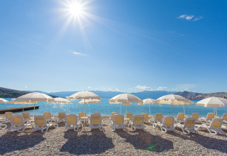 Tumbonas y sombrillas al sol en la playa de Valamar Camping Baška, Primorje-Gorski Kotar, Croacia.
