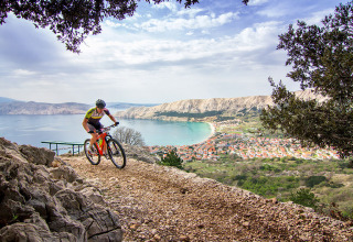 Ciclista su sentiero roccioso con vista su Baška e la baia in Primorje-Gorski Kotar, Croazia.