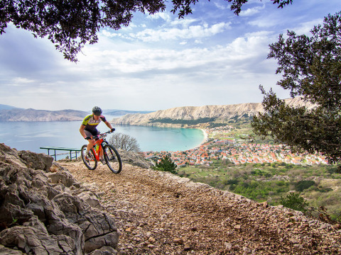 Ciclista su sentiero roccioso con vista su Baška e la baia in Primorje-Gorski Kotar, Croazia.