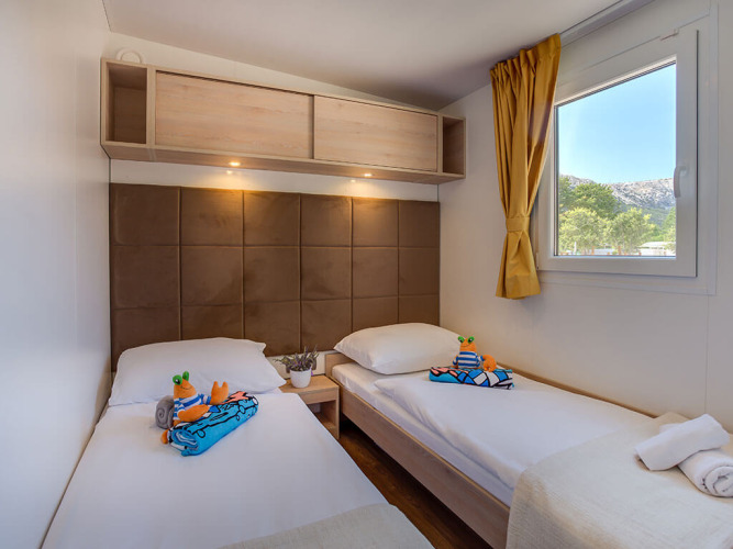 Chambre moderne à Vela Bay Home, Croatie, avec deux lits simples, jouets, fenêtre et étagère murale.