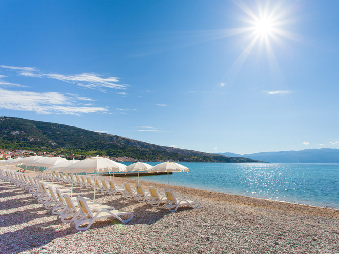 Zonnig strand met ligbedden en parasols bij Vela Bay Home, Valamar Camping Baška, Kroatië.