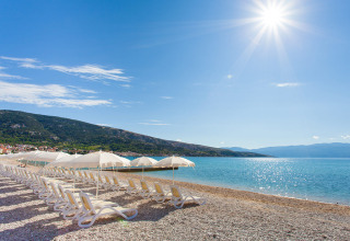 Solrig strand med liggestole og parasoller ved kysten, Vela Bay Home, Valamar Camping Baška, Kroatien.