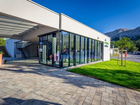 Bâtiment moderne aux murs de verre au Valamar Camping Baška, entouré de montagnes et verdure en Croatie.
