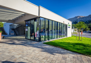 Bâtiment moderne aux murs de verre au Valamar Camping Baška, entouré de montagnes et verdure en Croatie.