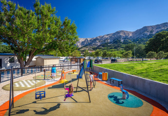 Parco giochi a Vela Bay Home presso Valamar Camping Baška, Croazia, con montagne sullo sfondo.