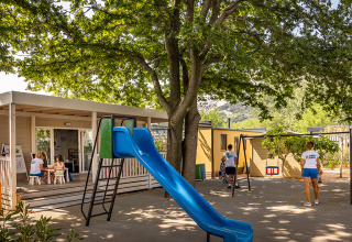 Playground with slide and swings under shady trees at Valamar Camping Baška holiday park in Croatia.