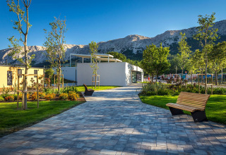 Allée pavée avec bancs, arbres et montagnes au parc de vacances Valamar Camping Baška en Croatie.