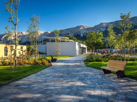 Paved path with benches, trees, and mountain backdrop at Valamar Camping Baška holiday park in Croatia.