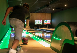 Persoon gooit een bowlingbal op een moderne bowlingbaan met groene verlichting in een vakantiepark.