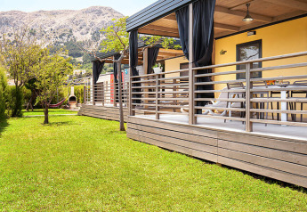 Sunny Beach Home met houten terras, groene tuin, hangmat en zicht op de bergen in de achtergrond.