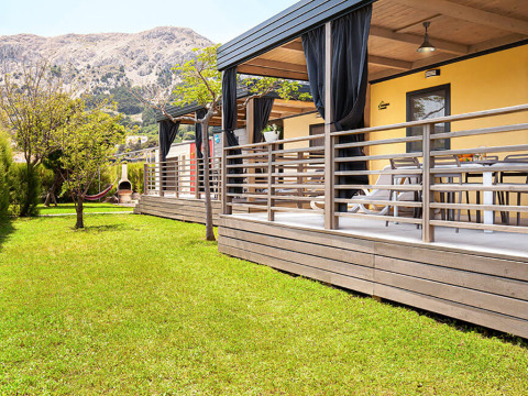 Lodge Sunny Beach Home con terraza de madera, césped verde, hamaca y montañas al fondo.
