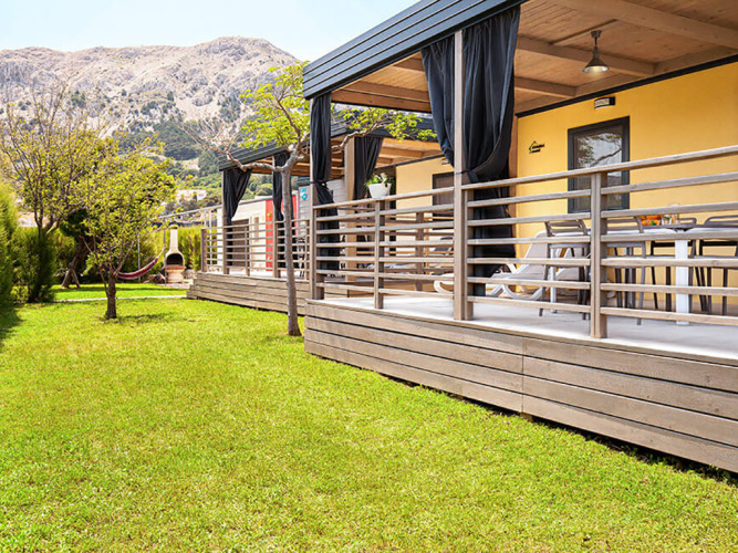 Sunny Beach Home met houten terras, groene tuin, hangmat en zicht op de bergen in de achtergrond.