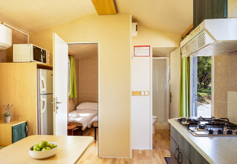 Interior of Brioni Home Seaside chalet showing cozy bedroom, kitchen area, and table at Camping Brioni, Croatia.