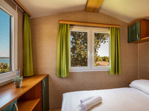 Chambre du chalet Brioni Home Seaside au Camping Brioni en Croatie avec rideaux verts et vue sur la nature.