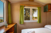 Camera da letto del chalet Brioni Home Seaside al Camping Brioni in Croazia con tende verdi e vista natura.