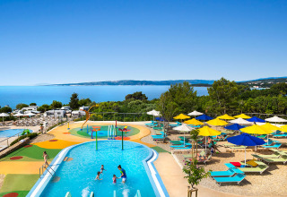 Kinderzwembad, kleurrijke parasols en zeezicht bij Valamar Camping Krk vakantiepark in Kroatië.