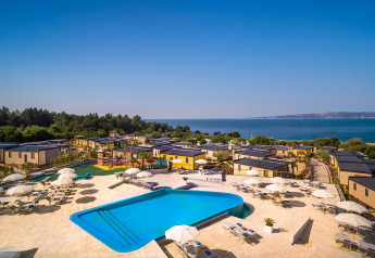 Vakantieoord met groot zwembad, ligzetels en parasols; bungalows vlak bij de kustlijn.
