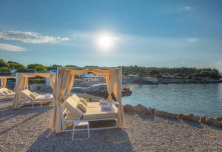 Letti a baldacchino su spiaggia di ciottoli davanti al mare a Valamar Camping Krk, Croazia, al tramonto.