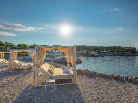 Sunlit canopy beds on a pebbled beach at Valamar Camping Krk, Croatia, overlooking the peaceful coastline.