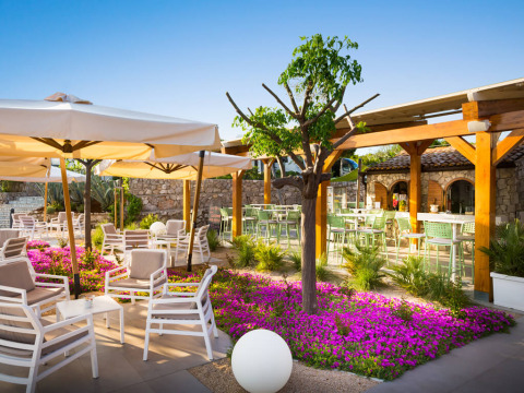 Buitenlounge bij Valamar Camping Krk in Kroatië met bloemenperk, parasols, witte stoelen en stenen muren.