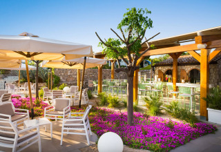 Außencafé im Valamar Camping Krk in Kroatien mit bunten Blumen, Sonnenschirmen und modernen Sitzplätzen.