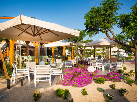 Outdoor dining area with white chairs, umbrellas, and flowers at Valamar Camping Krk in Croatia.