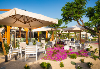 Buitenterras met witte stoelen, parasols en bloemen bij Valamar Camping Krk in Kroatië.