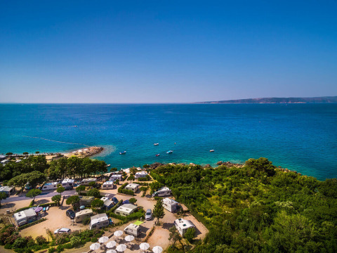 Wohnmobile am Meer nahe Krk in Kroatien, umgeben von grüner Natur und azurblauem Wasser unter klarem Himmel.