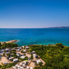 Campers aan de kust bij Krk, Kroatië, met prachtig blauw zeewater en groene, bosrijke omgeving zichtbaar.