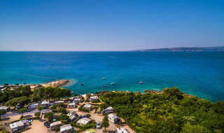 Campers aan de kust bij Krk, Kroatië, met prachtig blauw zeewater en groene, bosrijke omgeving zichtbaar.
