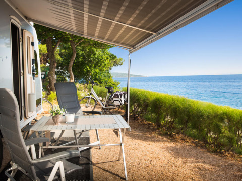 Seaside camping spot with RV, chairs, and table under awning at Valamar Camping Krk in Croatia.