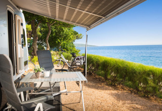 Campingplads ved havet med campingvogn, stole og bord under markise ved Valamar Camping Krk i Kroatien.