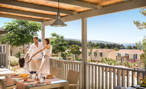 Familia disfruta del desayuno y el tiempo juntos en la terraza de Krk Home lodge con vistas al paisaje.