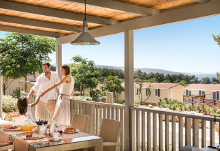 Familia disfruta del desayuno y el tiempo juntos en la terraza de Krk Home lodge con vistas al paisaje.