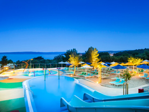 Beleuchteter Poolbereich mit Liegen und Sonnenschirmen bei Valamar Camping Krk in Kroatien am Abend.