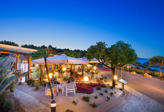 Buitenterras bij Valamar Camping Krk in Kroatië met zicht op zee, parasols en gezellige avondverlichting.