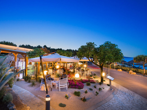 Outdoor dining area at Valamar Camping Krk in Croatia, featuring sea views, umbrellas, and evening lighting.