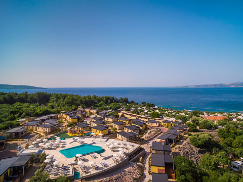 Aerial view of a lodge complex with a pool, umbrellas and sea view, surrounded by lush greenery