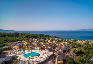 Luftfoto af moderne lodge med swimmingpool, parasoller og udsigt over havet, omgivet af grøn skov